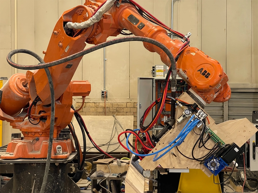 Orange ABB industrial robotic arm fitted with a custom end effector and bundled cables in a workshop setting.
